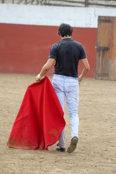 Back view of a bullfighter holding a red cape in an empty bullfighting arena.