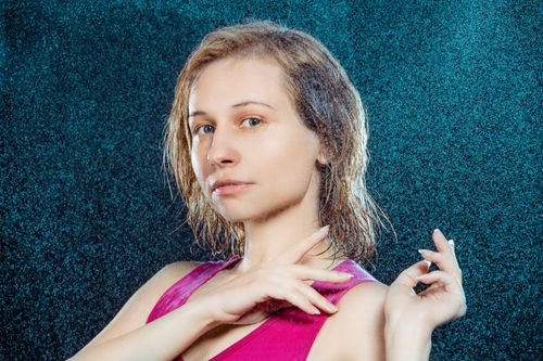 Free Portrait of young blonde female standing under falling water drops against blue background and looking at camera Stock Photo