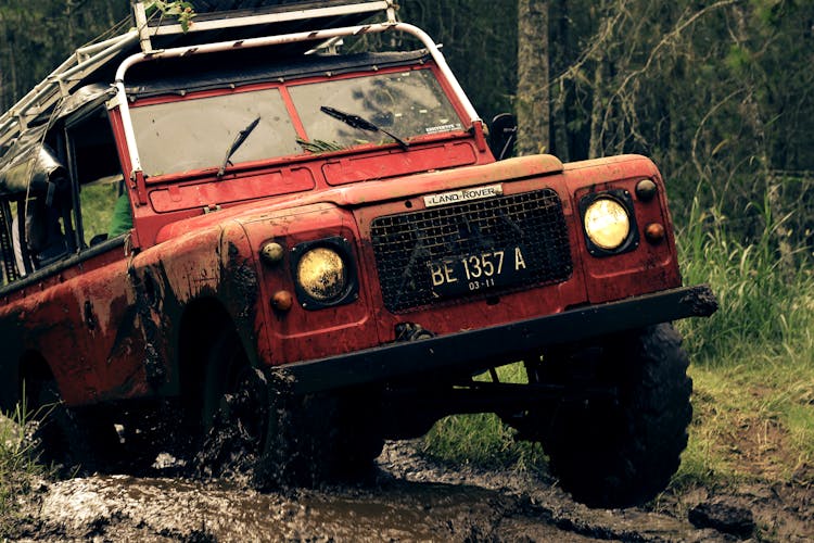 Red Car On Muddy Road Near Trees