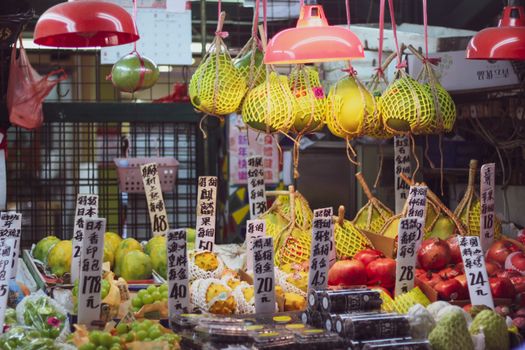 Colorful fruits and vegetables for sale under red lamps at a bustling Asian street market.