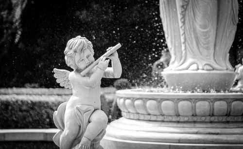 Free A grayscale close-up of a stone angel statue in a decorative water fountain. Stock Photo