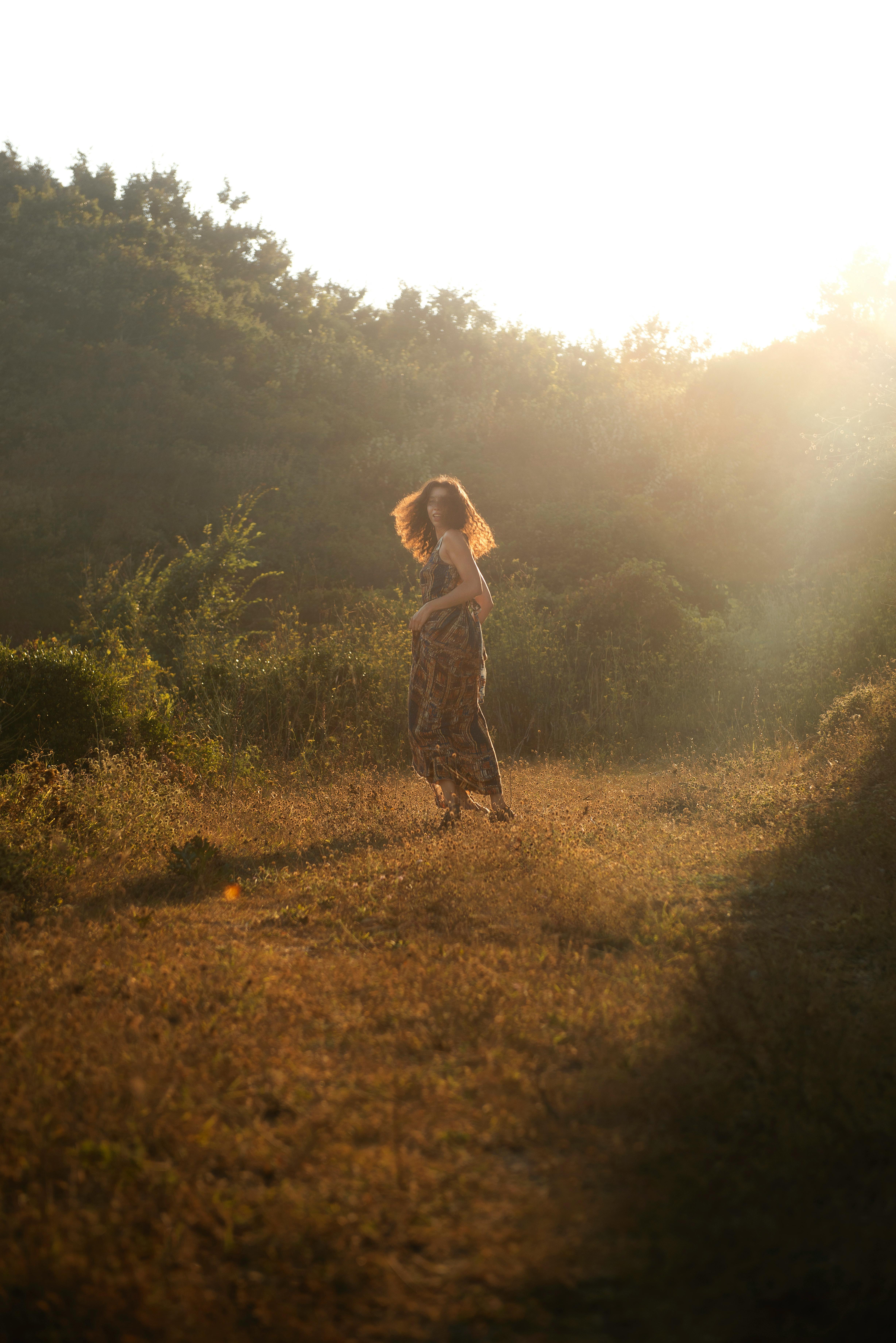 A serene scene of a woman walking in a sunlit field during sunrise, creating a peaceful ambiance.