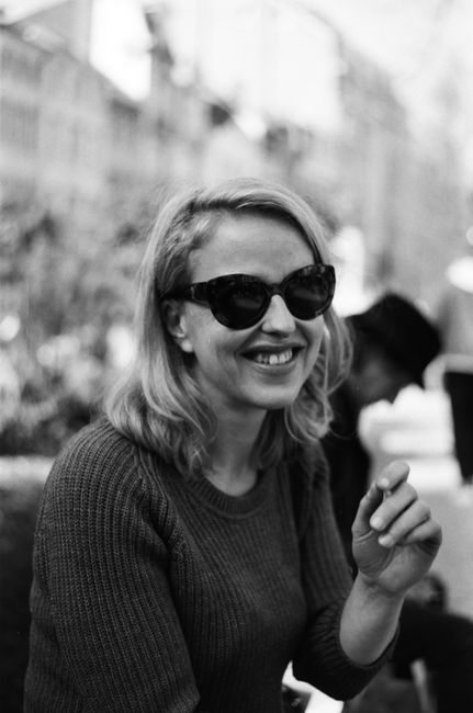 A stylish woman wearing sunglasses smiles outdoors in Liège, Belgium. Black and white portrait.
