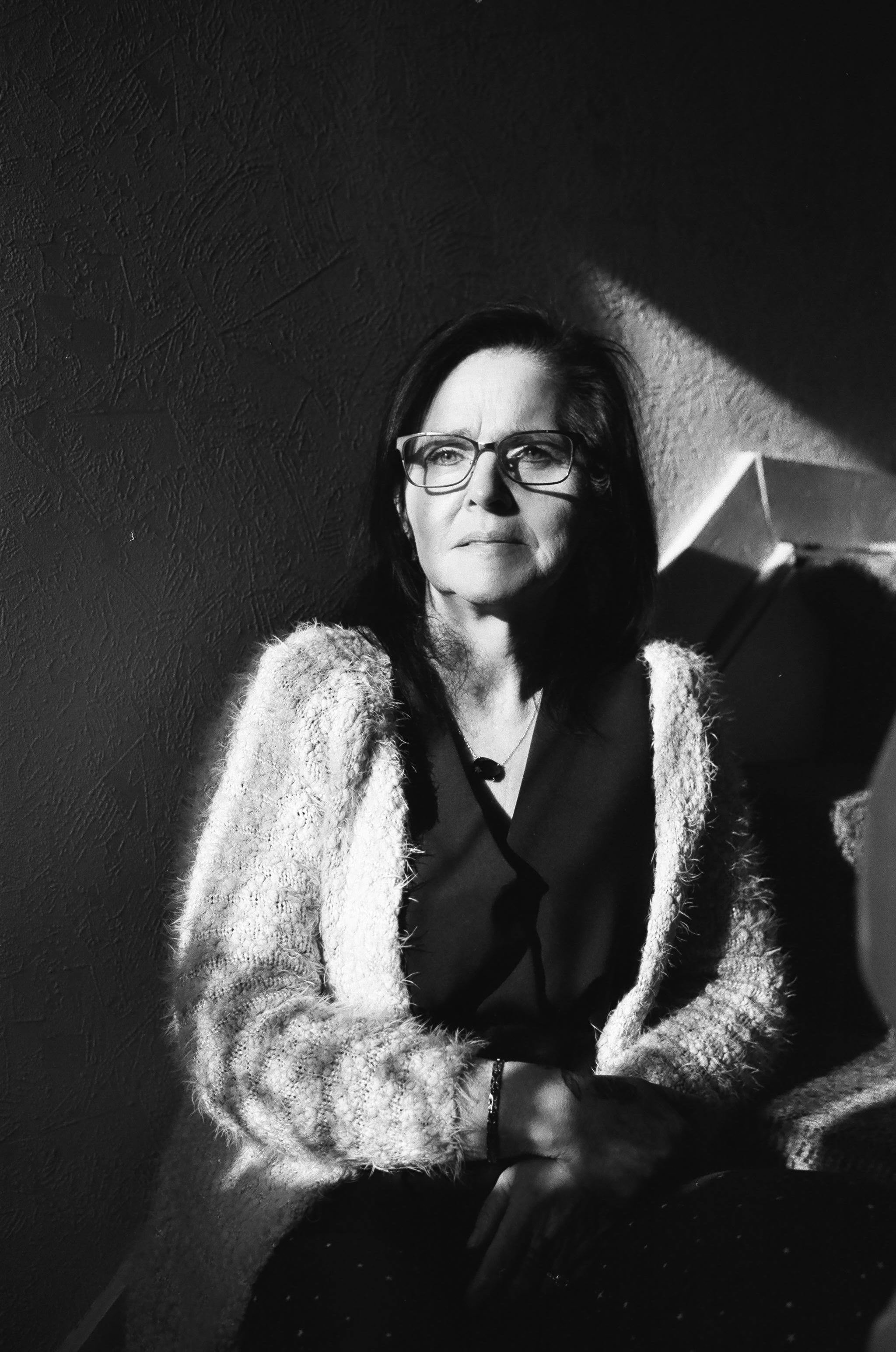 Elegant black and white portrait of a stylish woman sitting indoors with striking lighting.
