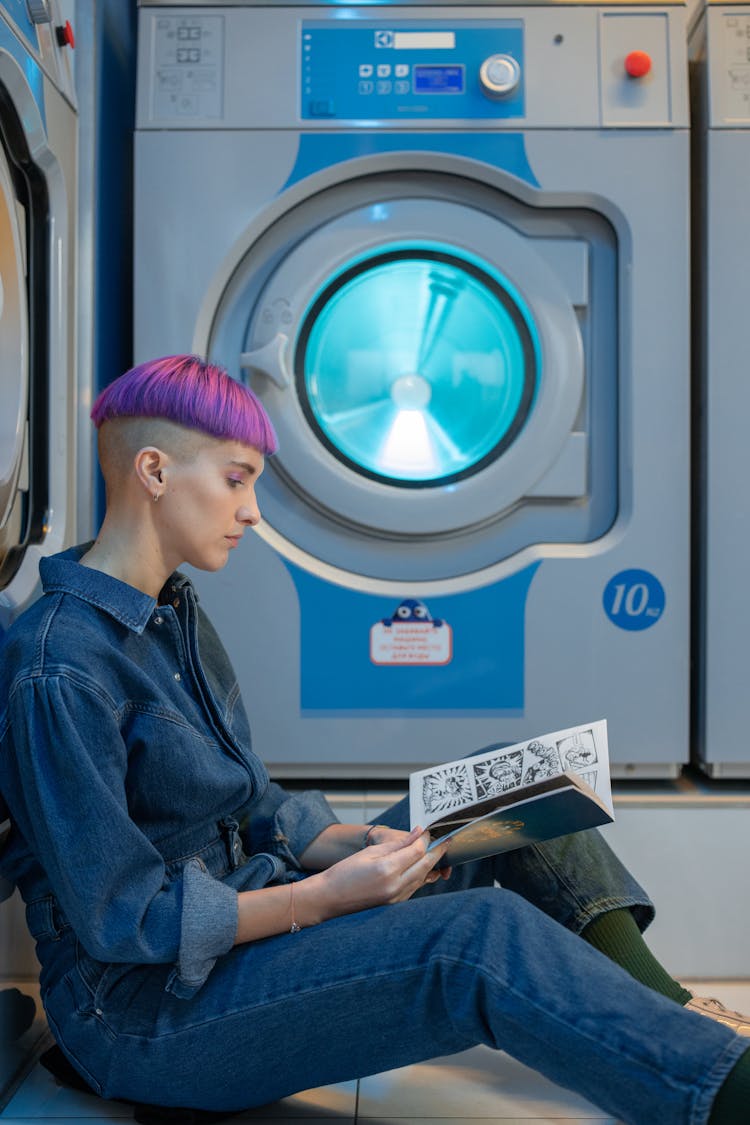 Person In Denim Jumpsuit Sitting On The Floor While Busy Reading Comics