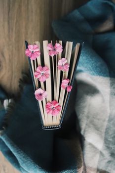 Top view of an open book adorned with pink flowers on a cozy blanket.