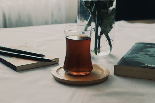 Free Aesthetic tea glass on a wooden coaster with books on a table, creating a cozy atmosphere. Stock Photo