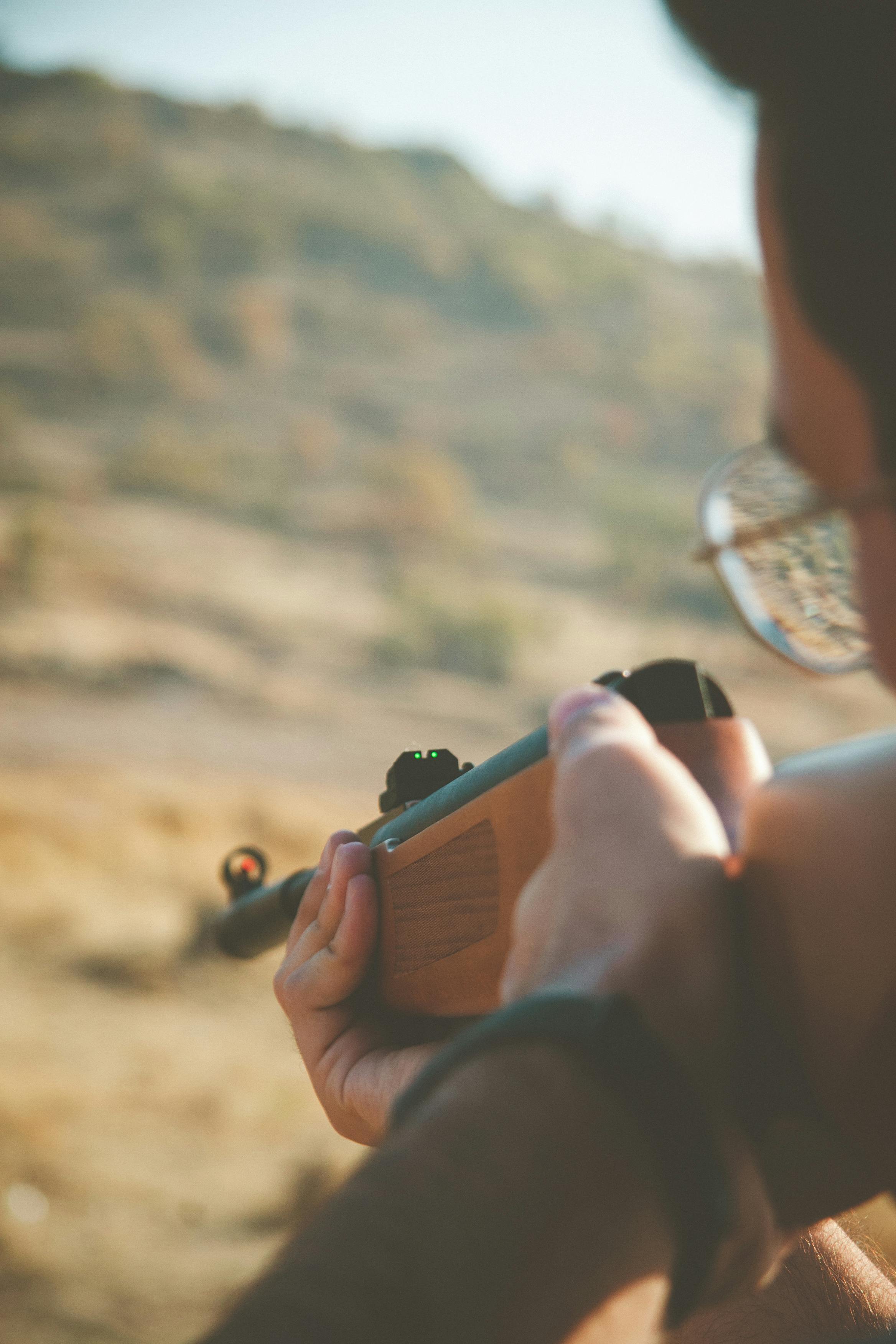 A close-up of a person aiming a rifle outdoors in a desert-like field in Kayseri, Türkiye.