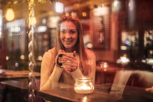 女人抱著坐在棕色的木桌附近的白色陶瓷杯