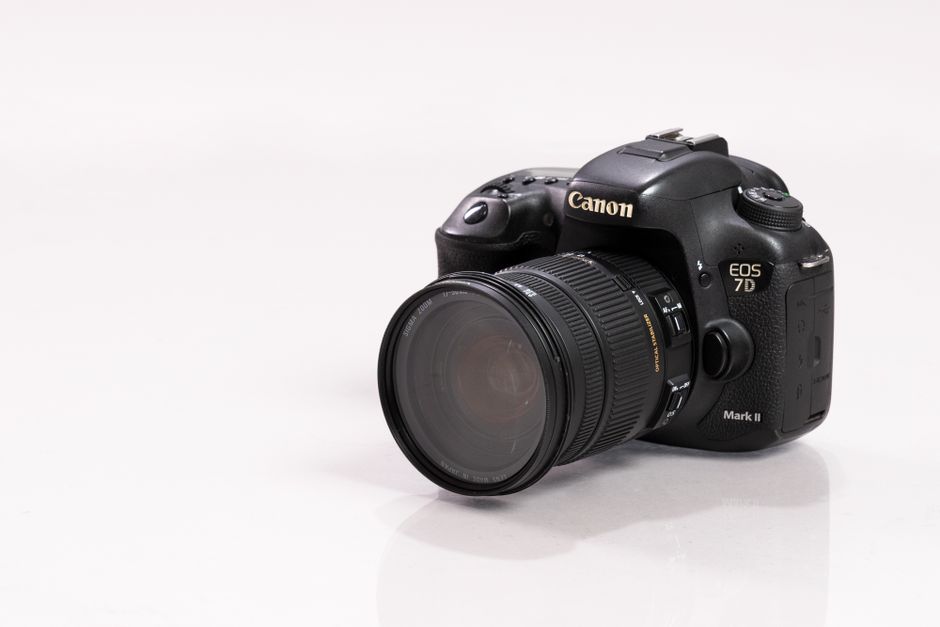 Close-up de uma câmera DSLR com lente acoplada em uma superfície branca, destacando equipamentos profissionais de fotografia.
