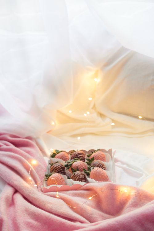 Free Elegant display of chocolate-covered strawberries on a pink blanket with string lights creating a cozy ambiance. Stock Photo