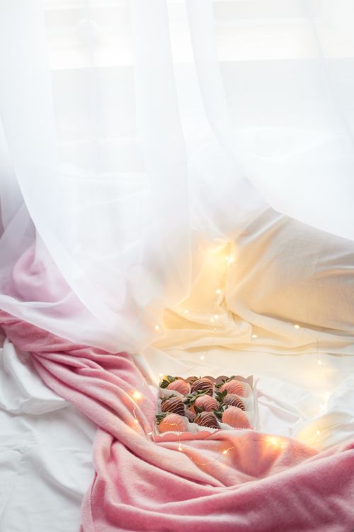 Free Romantic dessert arrangement with chocolate strawberries and fairy lights on soft pink fabric. Stock Photo