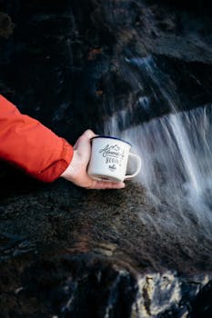 苏格兰高地的瀑布下，有人手持杯子，冒险正等待着
