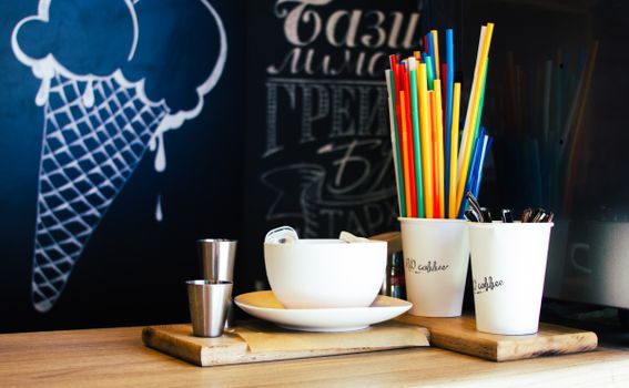 Vibrant coffee shop setup with colorful straws and cups on a wooden counter, featuring a chalkboard wall.