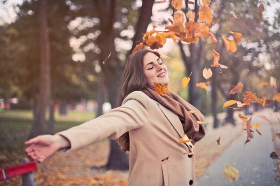 Woman standing outdoors among falling autumn leaves — photo by Andrea Piacquadio on Pexels