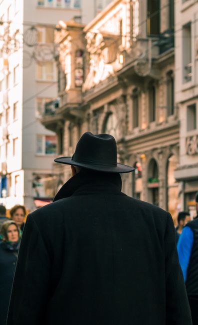 Back view of unrecognizable man near people walking on town street near aged buildings in daytime