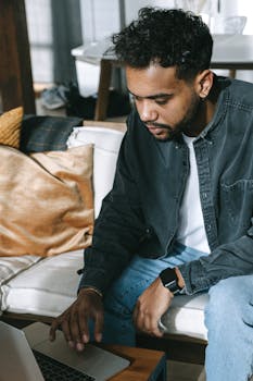 A focused young man working remotely on his laptop in a cozy home setting, embodying the digital nomad lifestyle.