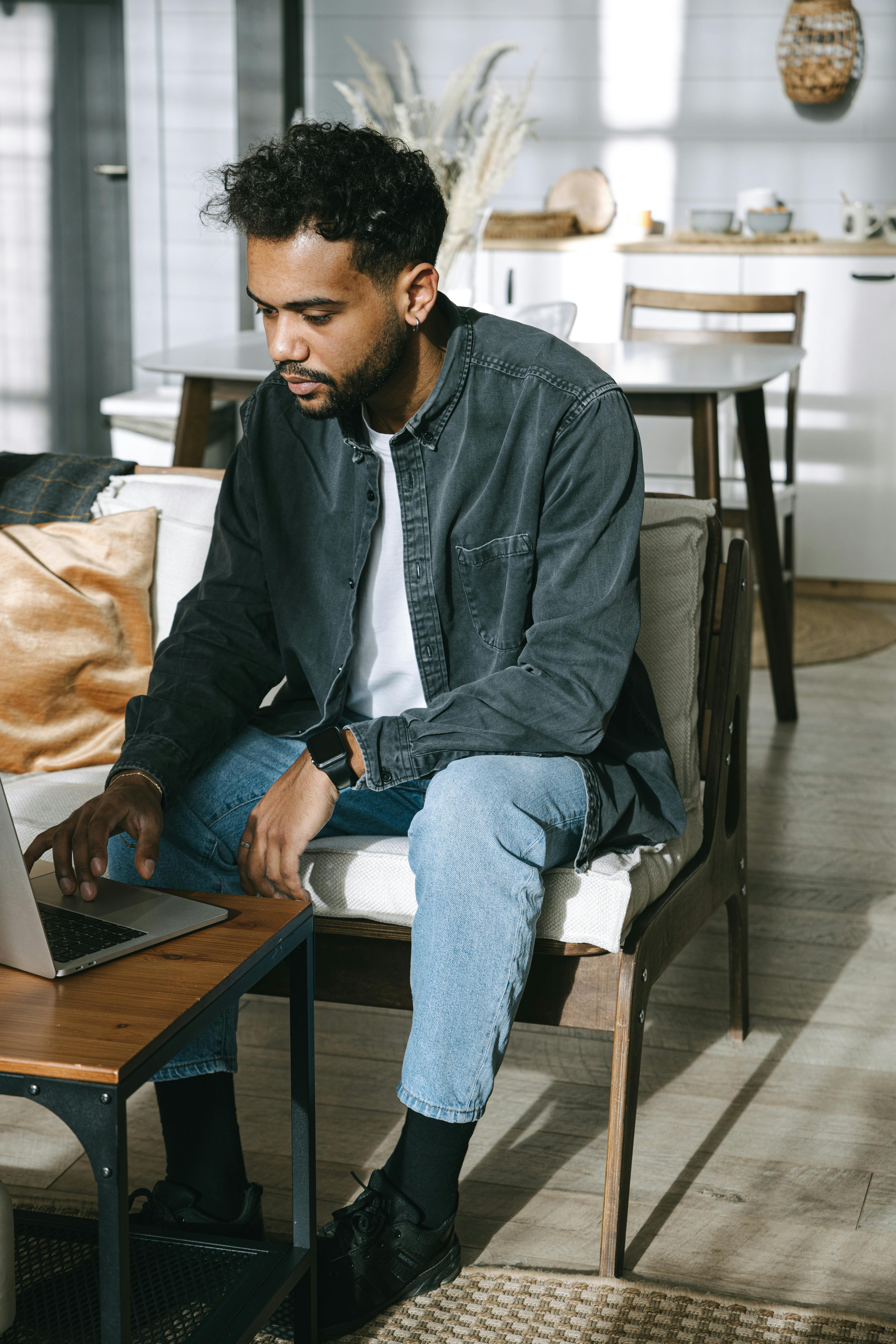 a man in black denim jacket busy browsing the laptop on the table