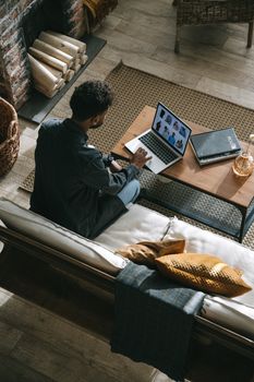A man works remotely on a laptop in a cozy living room setting, showcasing digital nomad lifestyle.