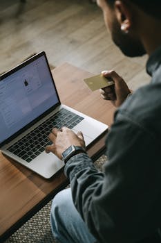 Young adult making an online purchase using a laptop and credit card indoors.