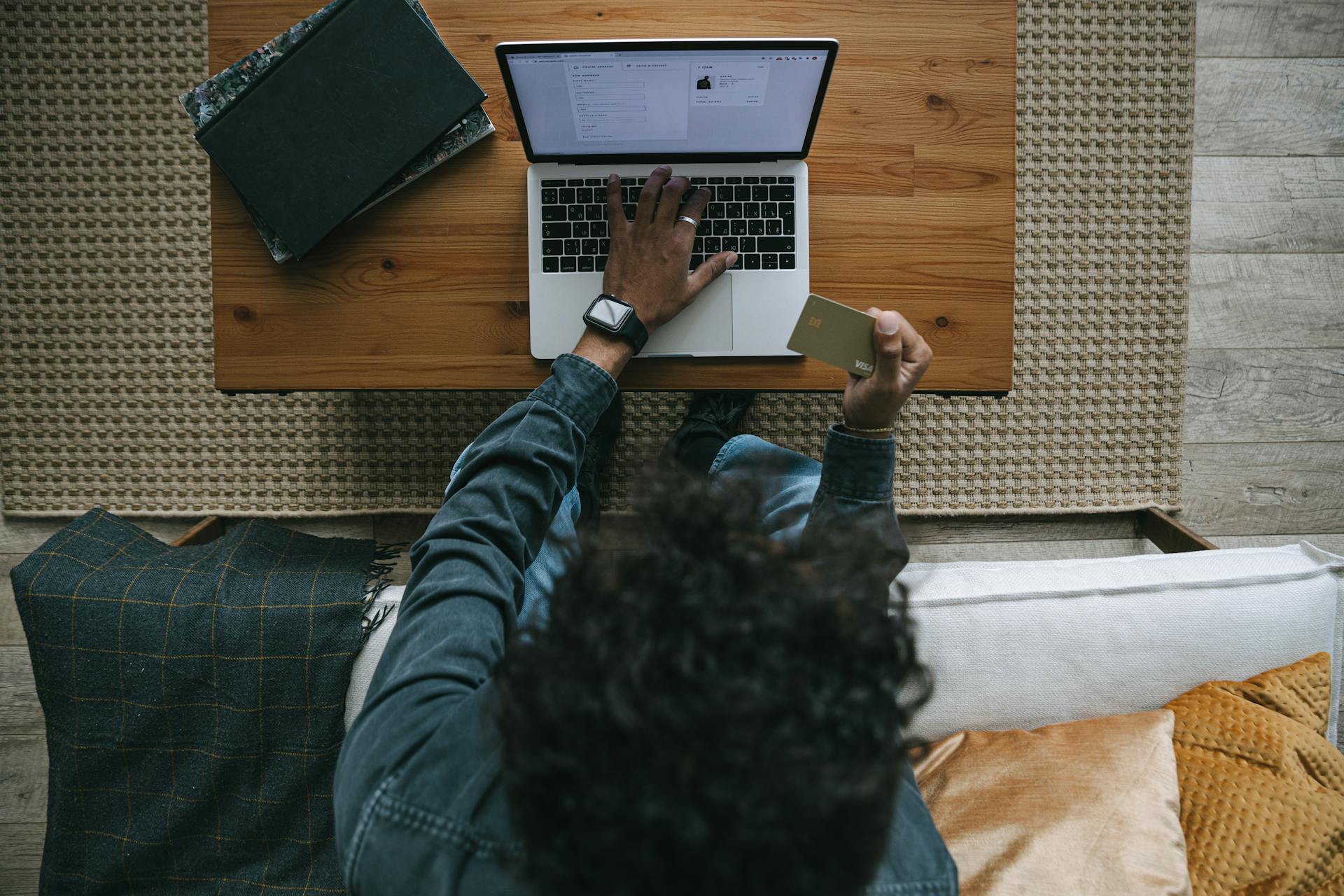 Adult man engaging in online shopping using a laptop and credit card on a wooden table.