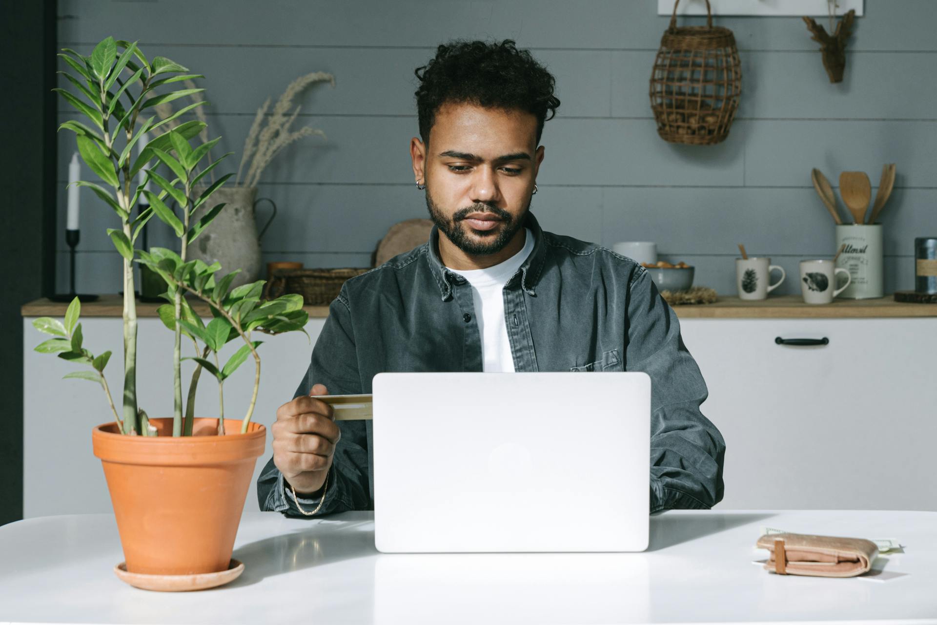 Man in denim jacket using credit card and laptop for online shopping at home.