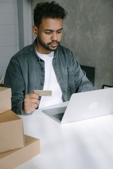 Young man using laptop and card for online shopping at home.