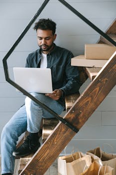 Man sitting on wooden stairs using laptop, symbolizing remote work lifestyle in a cozy setting.