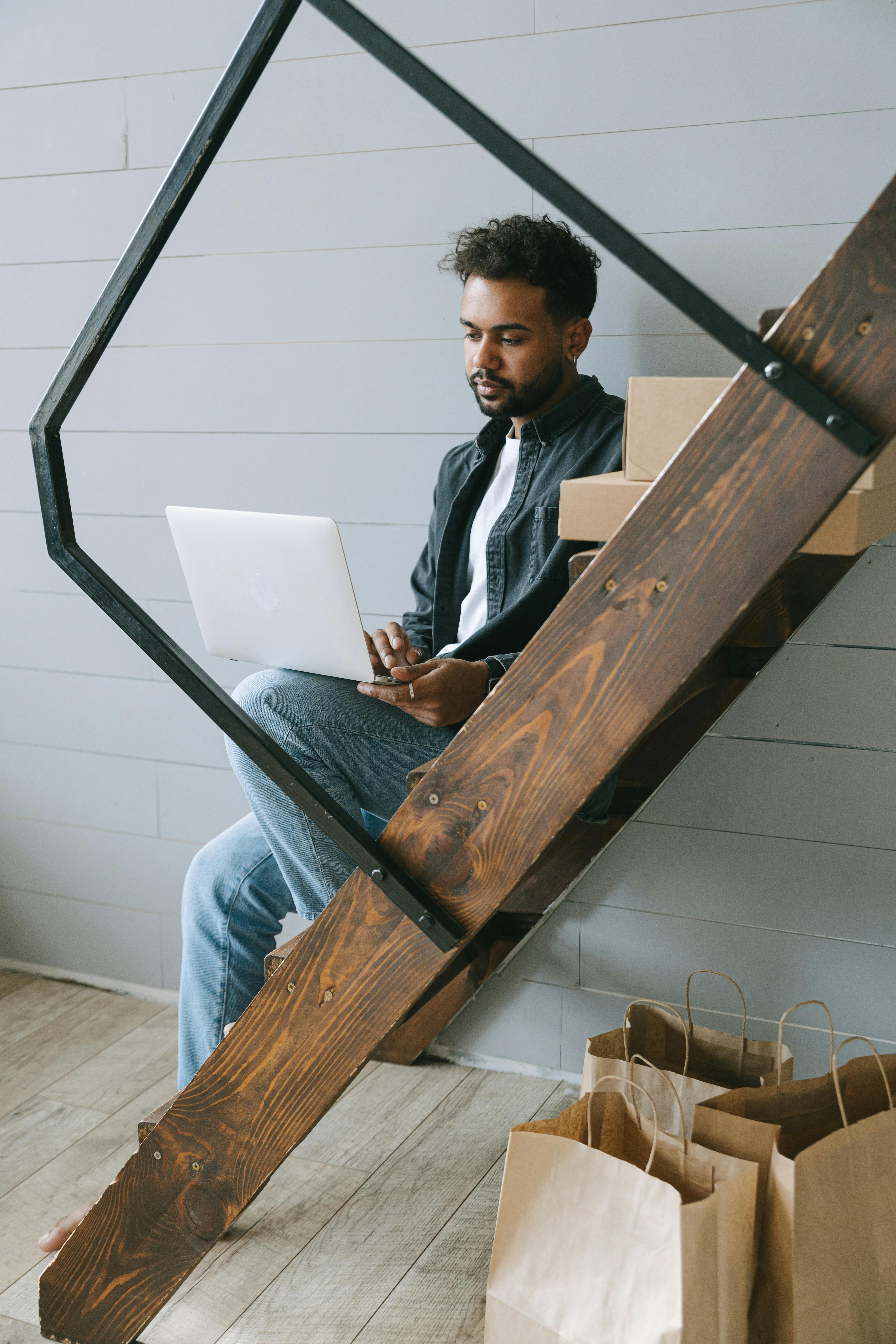 Man sitting on wooden stairs using a laptop for remote work in a modern home setting.