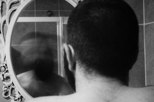 Free A Grayscale of a Man Looking at a Mirror Stock Photo