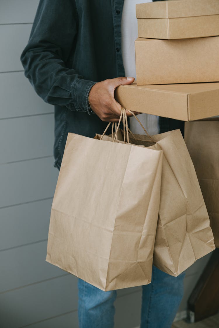 A Person In Black Denim Jacket Holding Stacks Of Boxes And Paper Bags