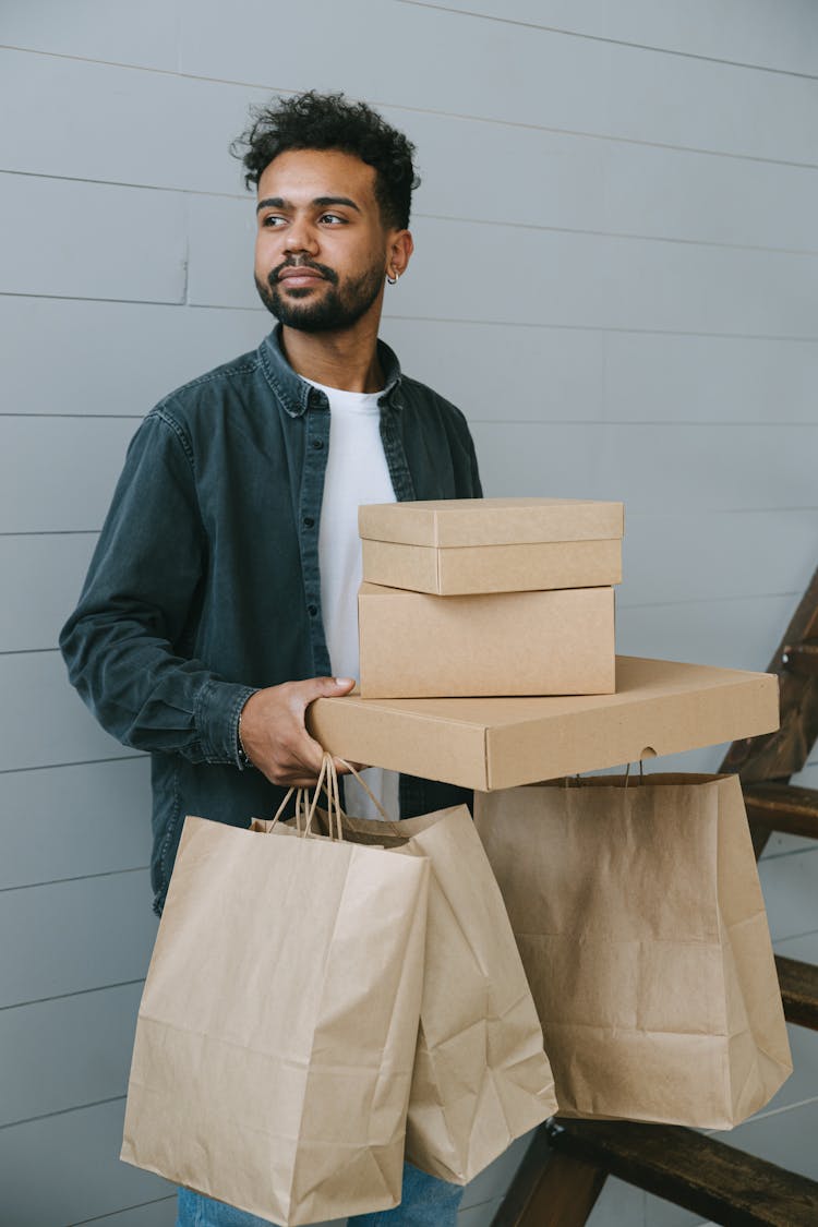 A Bearded Man Holding Stack Of Boxes And Paper Bags While Looking Afar