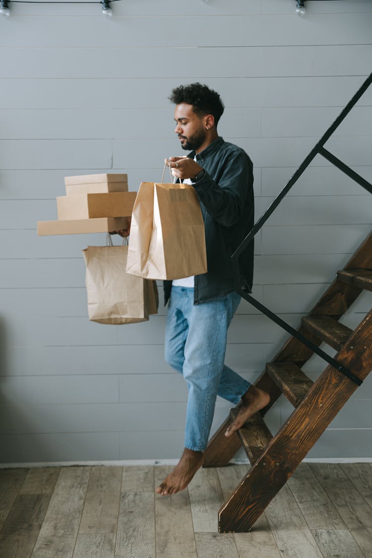 A Man Carrying Boxes And Paper Bags While Going Down The Stairs