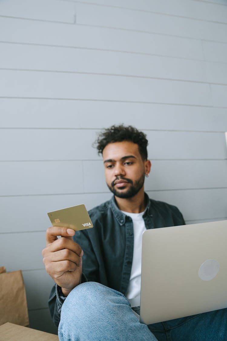 A Man In Black Denim Jacket Looking At The Visa Card He Is Holding