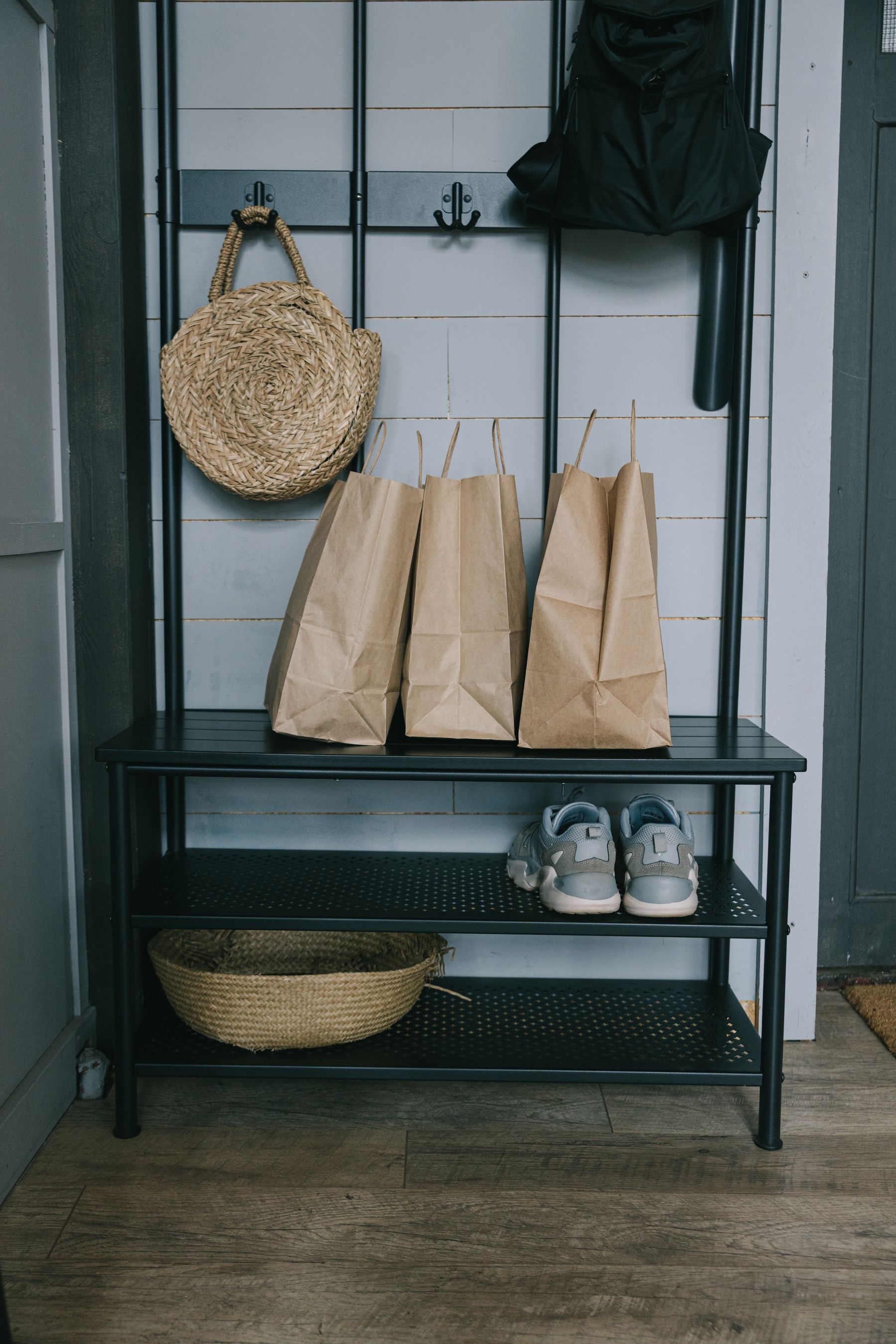 Entryway organized with a metal storage rack, shoes, woven baskets and household bags