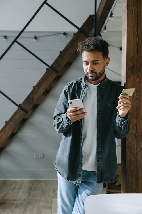 Man in Denim Jacket Holding Cellphone and a Card