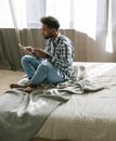Man in White and Black Plaid Dress Shirt and Blue Denim Jeans Sitting on Bed