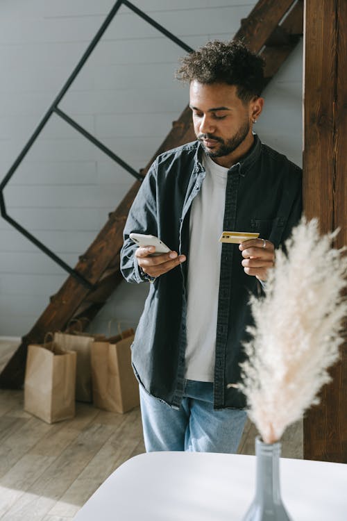 Person in Denim Jacket Holding Cellphone and a Card