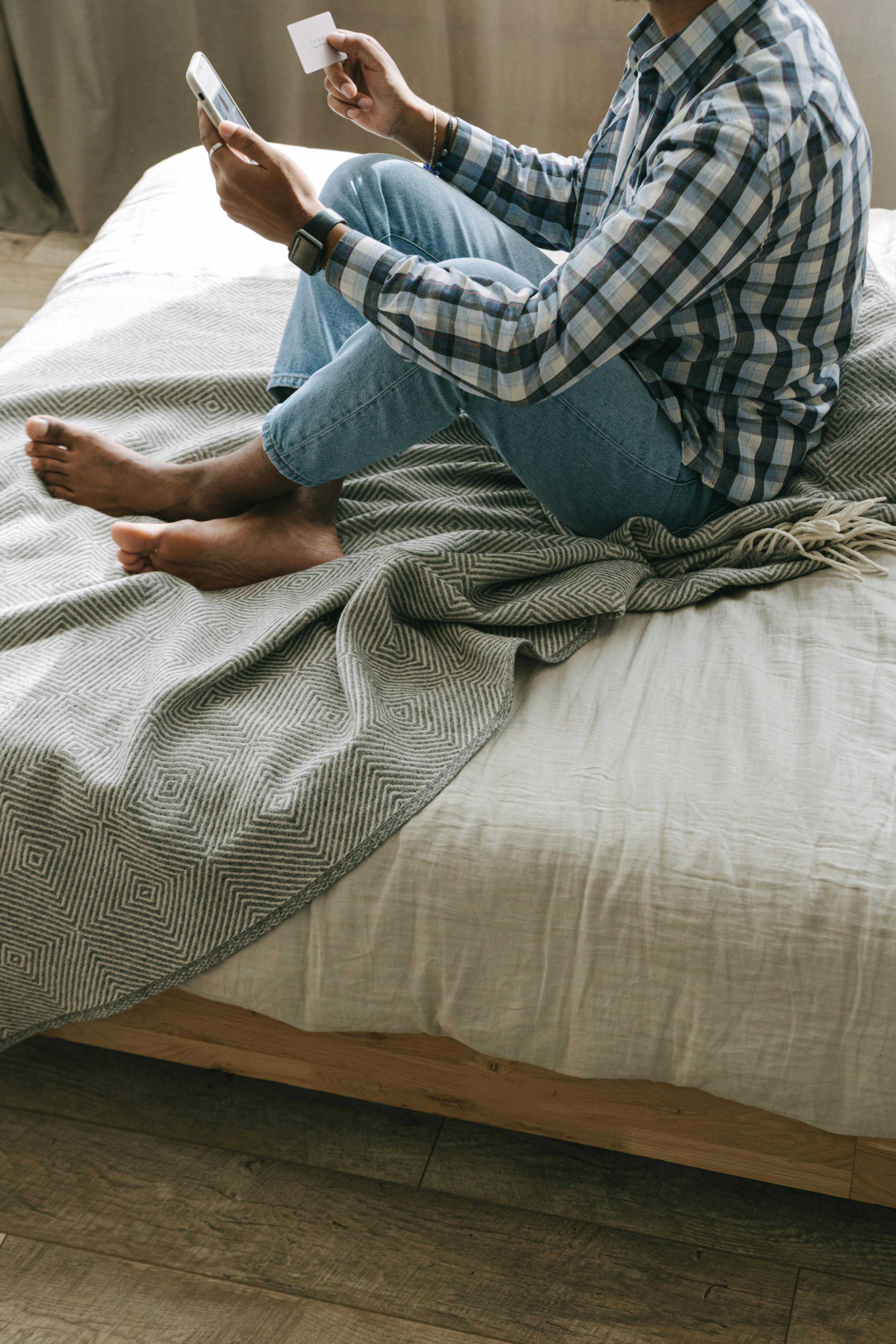 a person in plaid long sleeves sitting on the bed while busy using cellphone