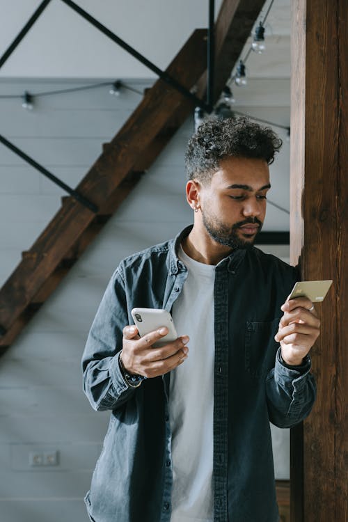 A Man Leaning on the Wooden Wall while Busy Looking at the Visa Card he is Holding