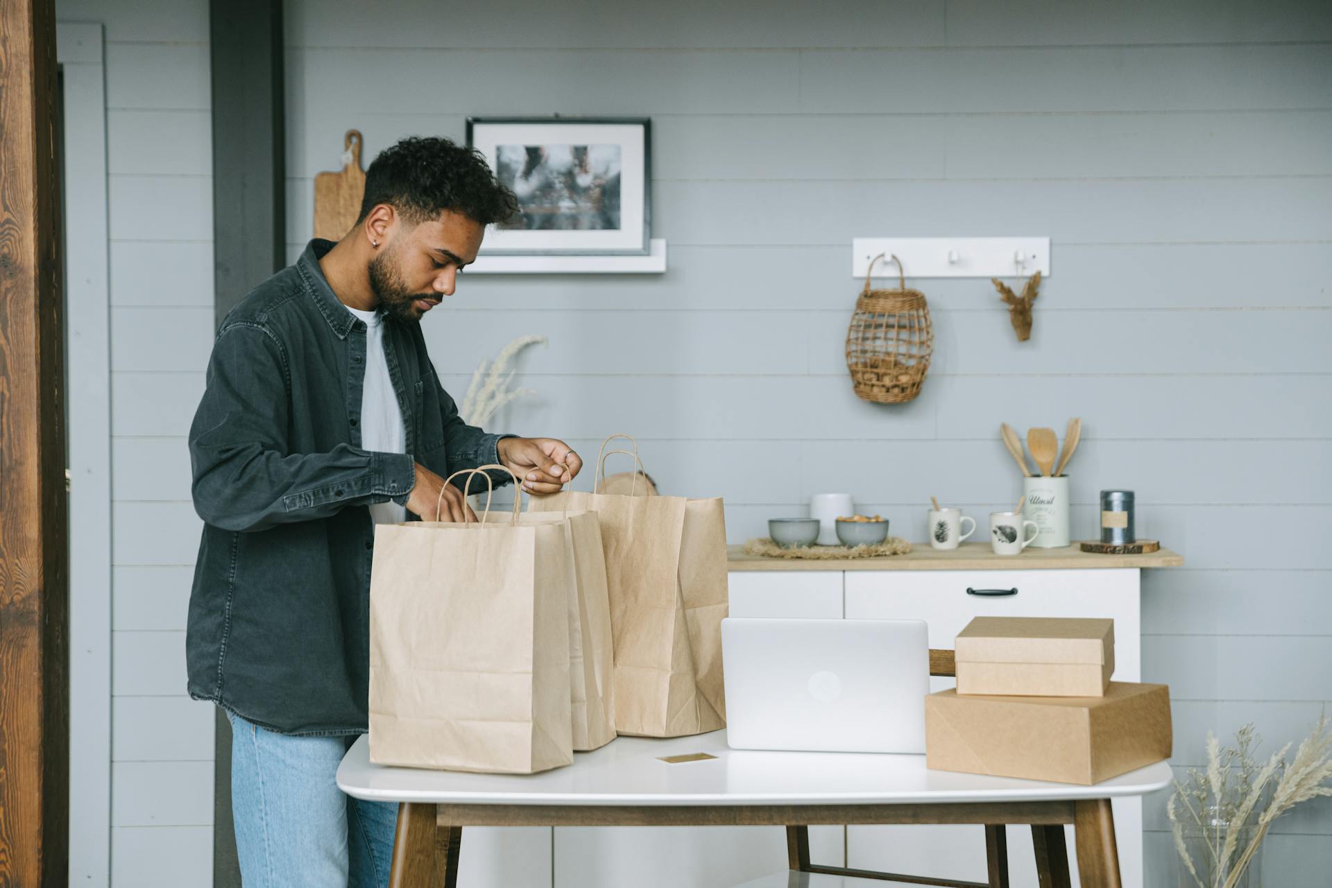 Man handling shopping bags and packages at a table indoors, showcasing a casual lifestyle scene.
