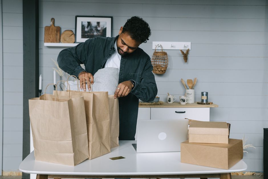 Young man organizing paper bags near a laptop in a cozy indoor setting. Young man organizing paper bags near a laptop in a cozy indoor setting.