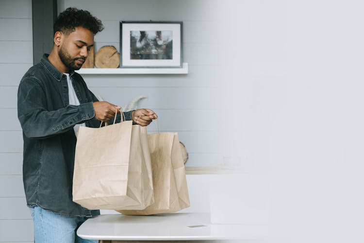 Man Carrying Paper Bags Near A White Table