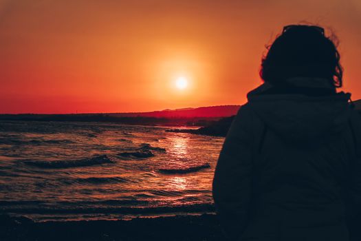 A serene beach sunset with a silhouette of a person, offering a dramatic view of the ocean waves.