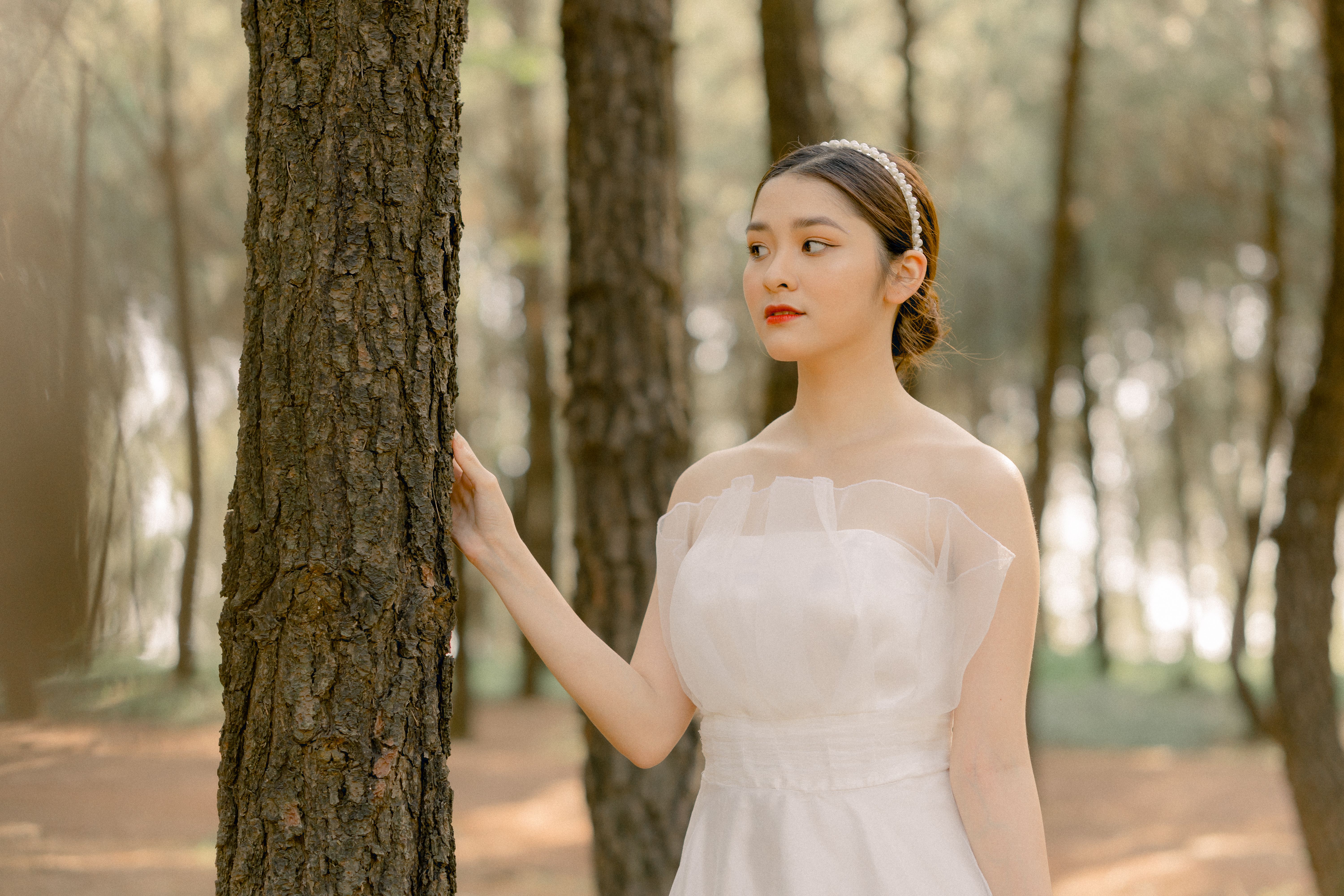 Beautiful bride in a white dress admires nature in a forest setting.
