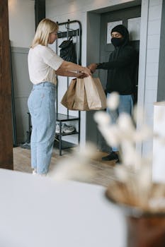 A woman receives a delivery package from a courier at her doorstep inside a modern home.