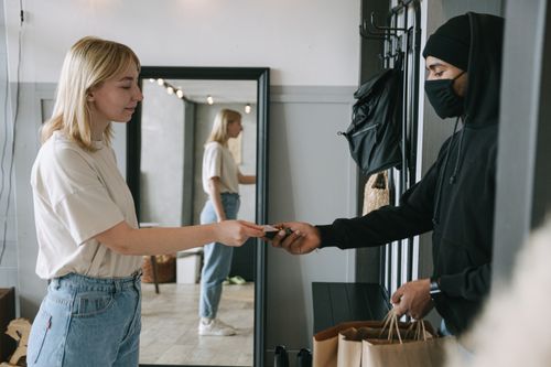 Free A woman receives a delivery and makes a contactless payment to a masked courier at home. Stock Photo