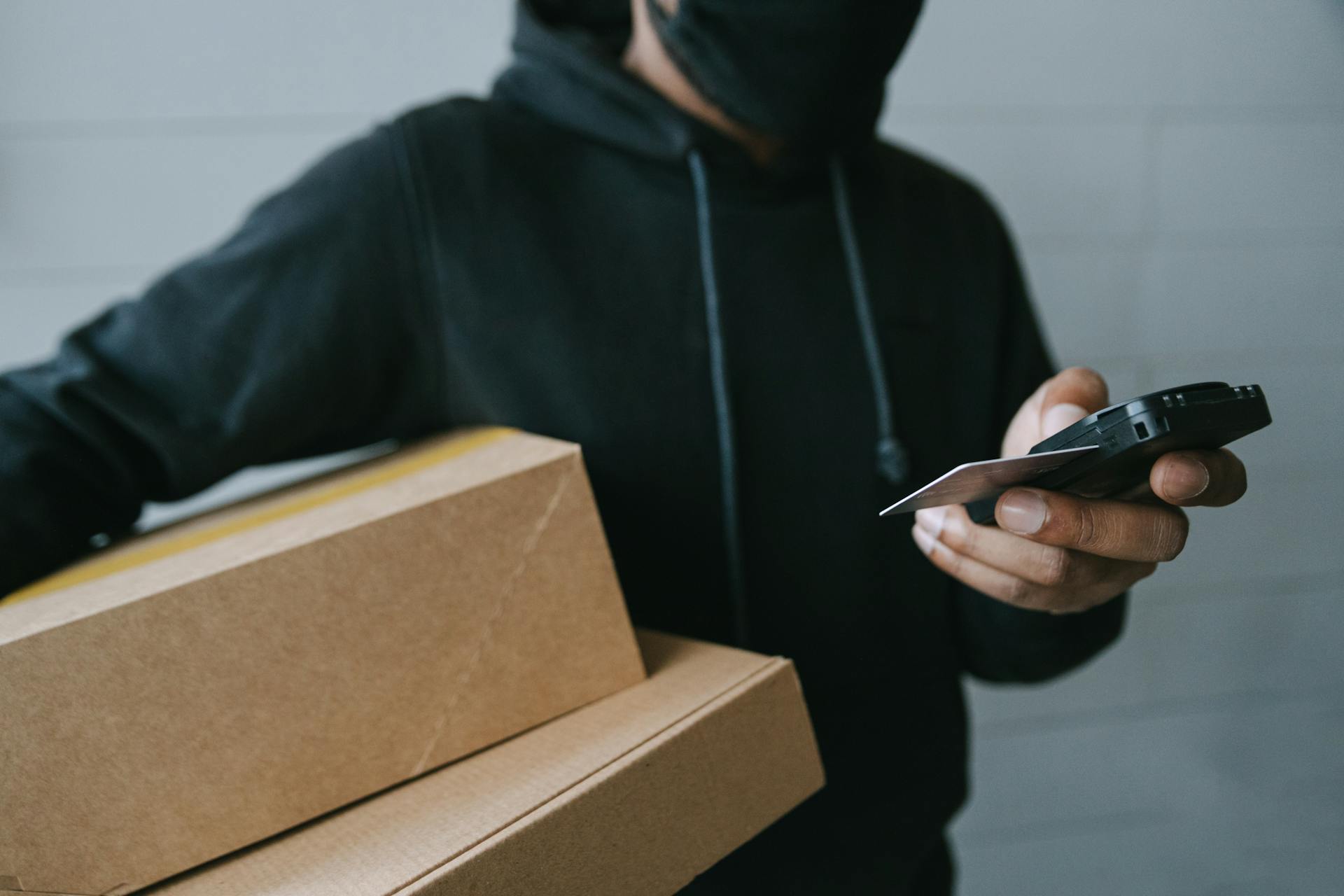 A Close-Up Shot of a Person in a Black Hoodie Holding Boxes while Using a Terminal