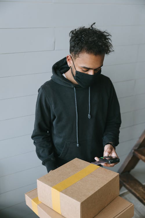 A Man Using a Payment Terminal while Carrying Cardboard Boxes