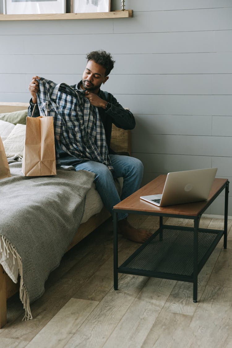 A Man Looking At A Plaid Shirt While Sitting On A Bed